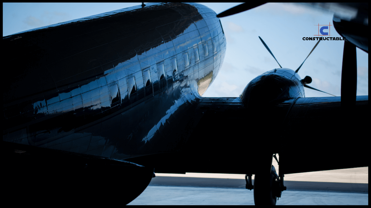 Silhouette of a vintage aircraft with a shiny fuselage under a blue sky, partial view from behind focusing on the tail and rear fuselage during its ascent, with soft light illuminating its curves.