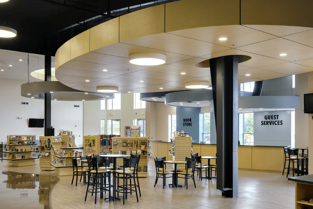 Modern public space featuring a bookstore and guest services area, with circular lighting fixtures overhead and tables with chairs for seating.