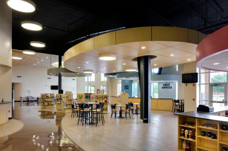 Modern library interior with bright lighting, circular desks, bookshelves, and an interview services area, featuring a polished floor and high ceilings.