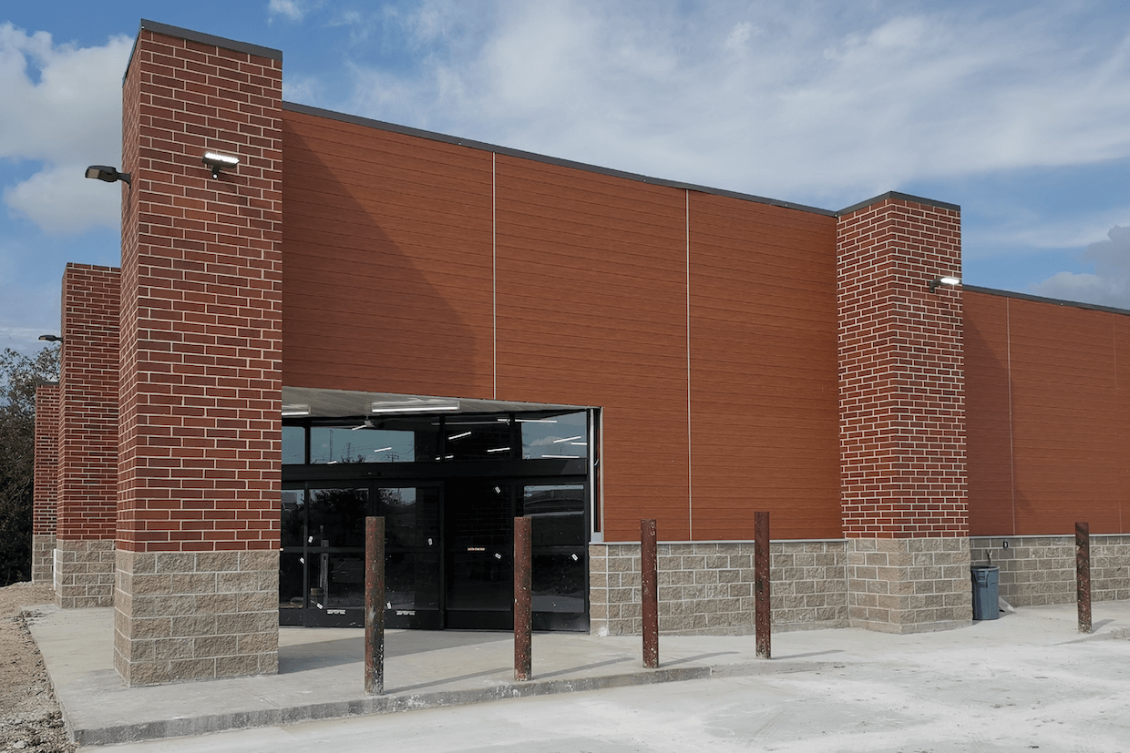 A modern building with a red brick and dark stone facade featuring a large glass door entrance, under a clear blue sky.