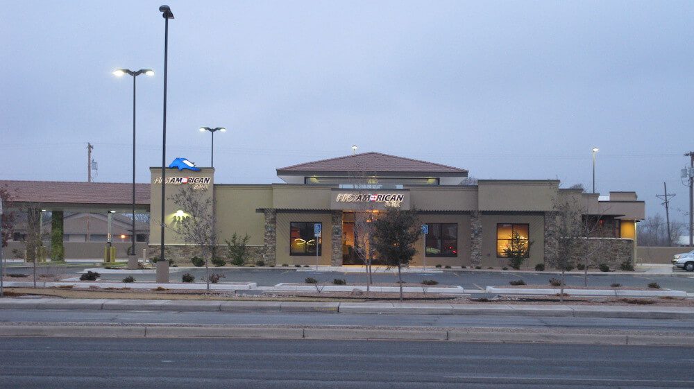 Exterior view of a modern chase bank branch during twilight, featuring lit windows, a prominent logo, and a sparse, tree-lined landscape along a street.