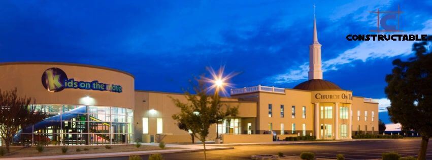 Exterior view of a modern church building at twilight with illuminated signage, featuring a large dome and spire, and a children's center called "Kids on the Move." The construction costs were carefully managed