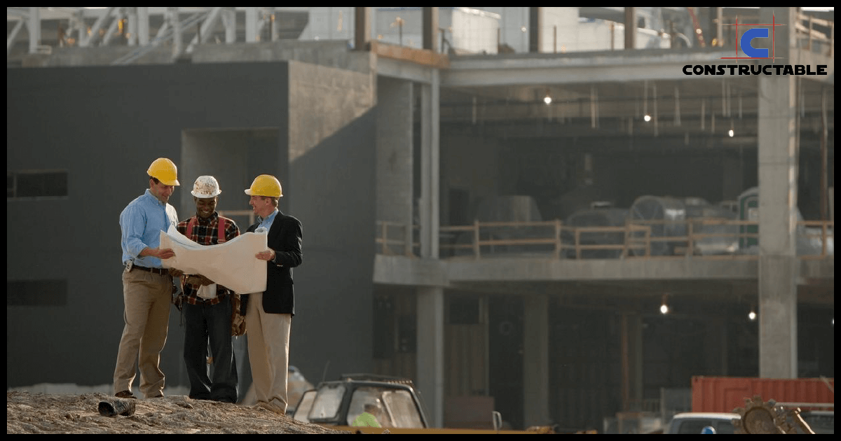 Three construction workers discussing construction costs and blueprints at a large construction site, with unfinished buildings in the background. The logo "constructable" is in the top right corner.