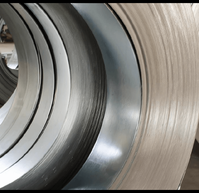 Large coils of shiny metal sheets, crucial in managing construction costs, are stored in an industrial warehouse, displaying different sizes and positioned to show curved edges. The constructable logo is visible in the corner.