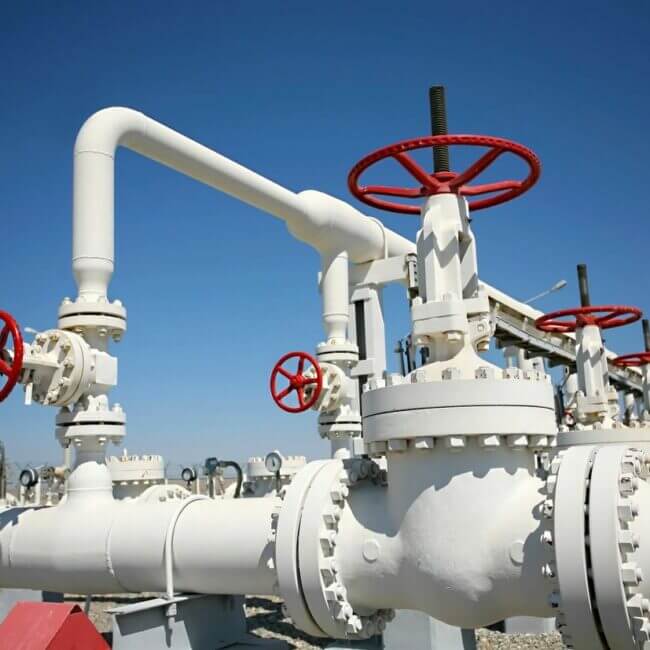 Industrial gas pipeline with multiple red valves and white pipes against a clear blue sky.