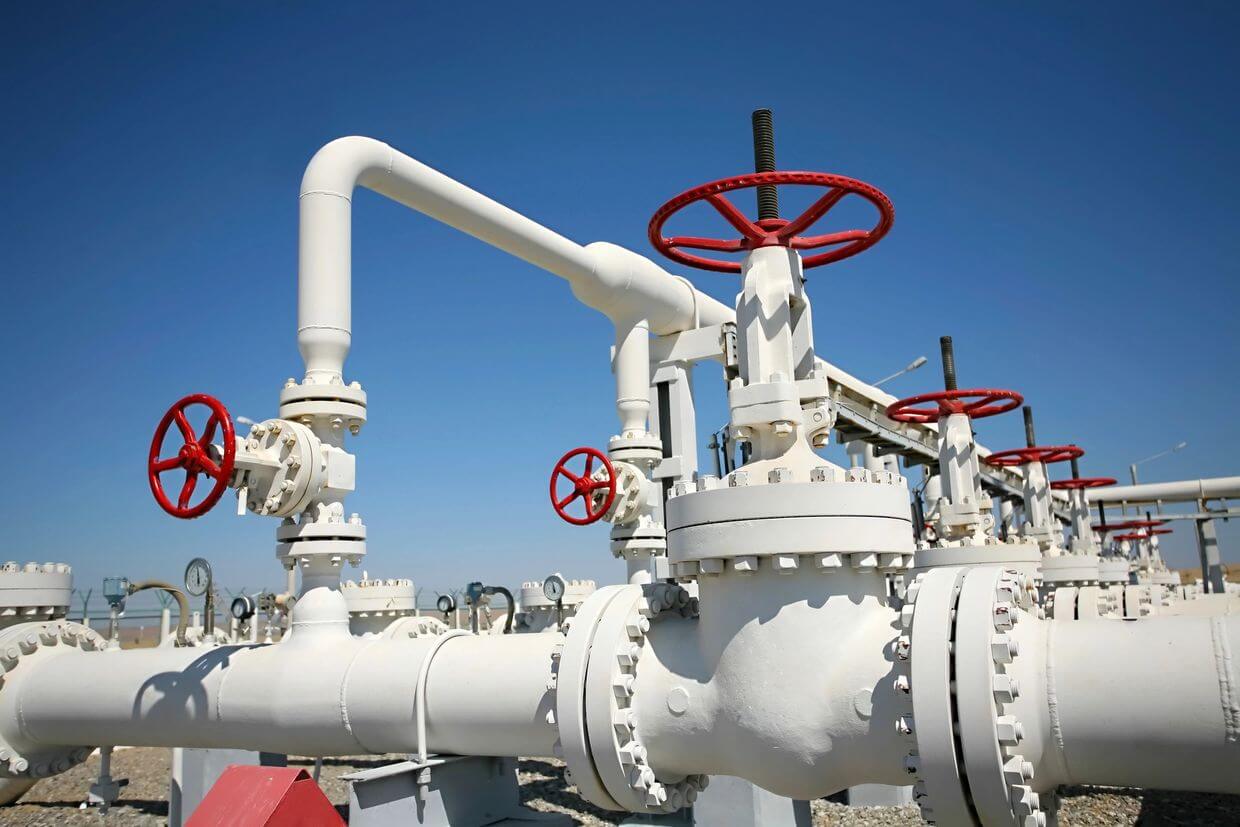 Industrial gas pipeline with multiple red valves and white pipes against a clear blue sky.