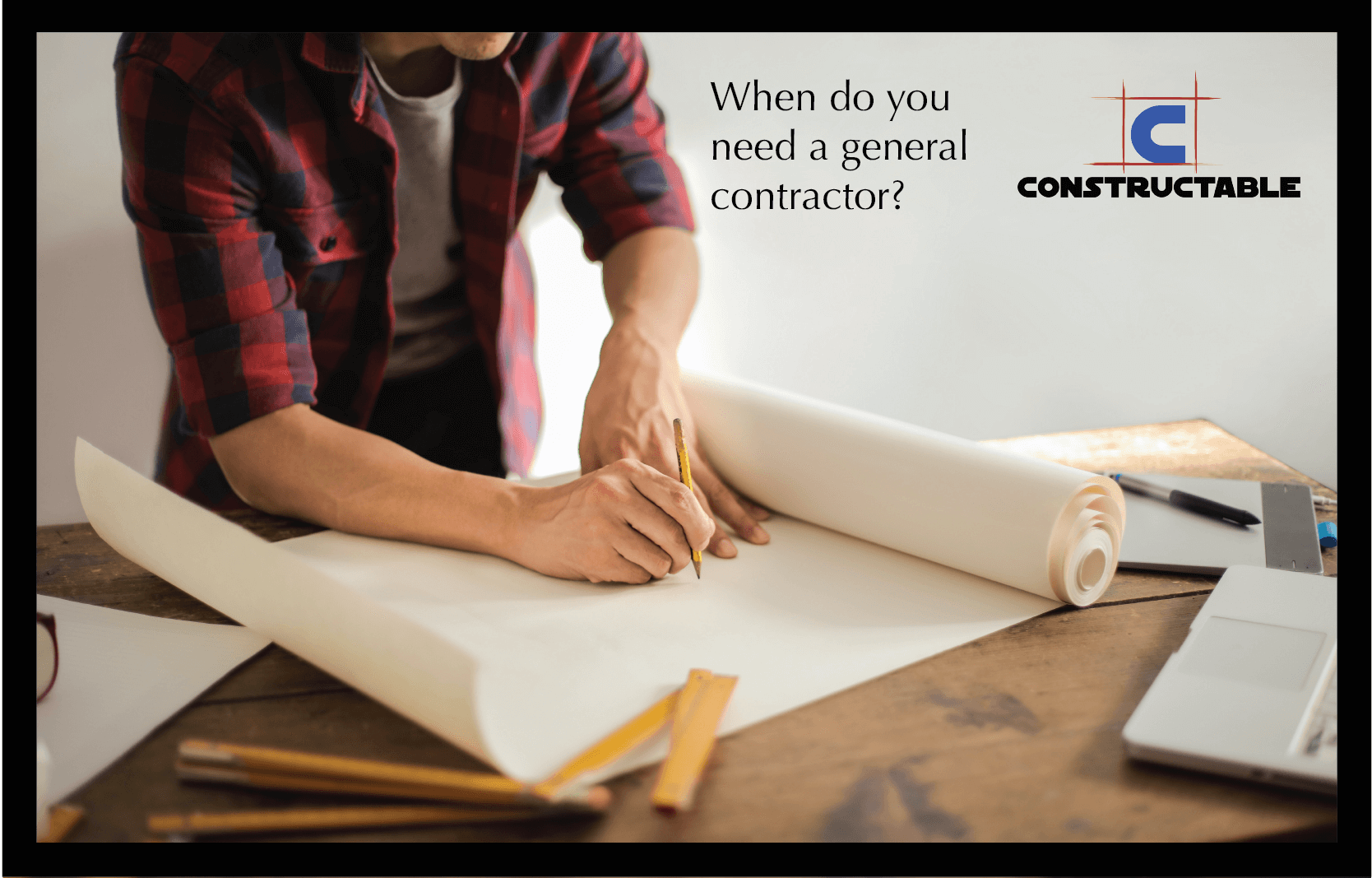 An architect in a plaid shirt working on construction costs and building plans at a desk with a laptop, smartphone, and construction tools. Text and logo of "constructable" in the top right corner