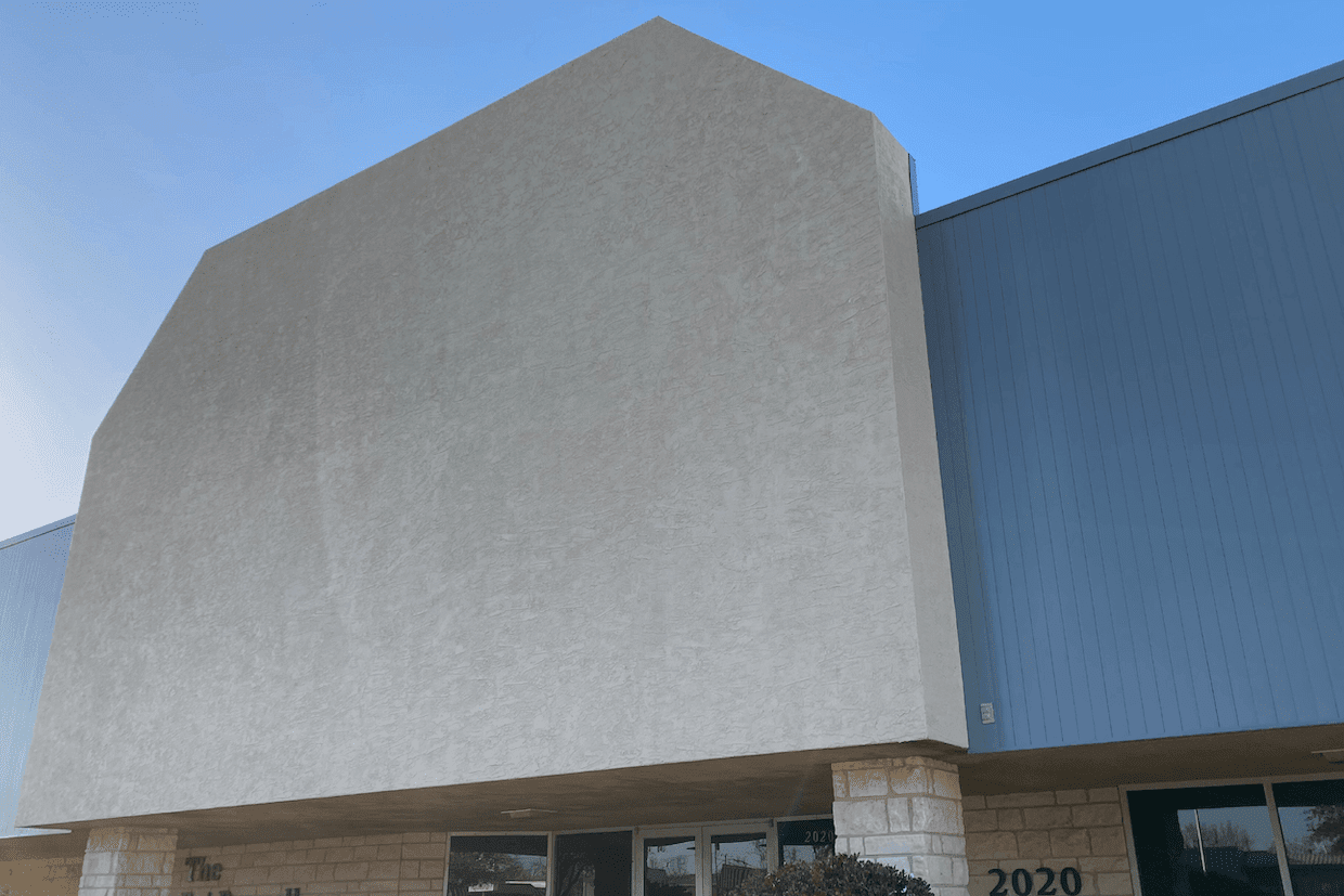 A modern building with a unique geometric shape, featuring a large, blank facade and textured walls under a clear blue sky. the numbers "2020" are visible on one part of the building.