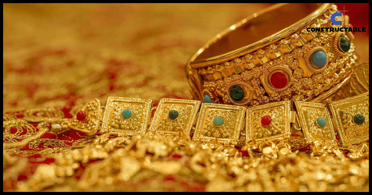A collection of traditional Indian jewelry featuring gold bracelets with intricate designs and embedded with various colorful gemstones, displayed on a rich, red fabric influenced by construction costs.
