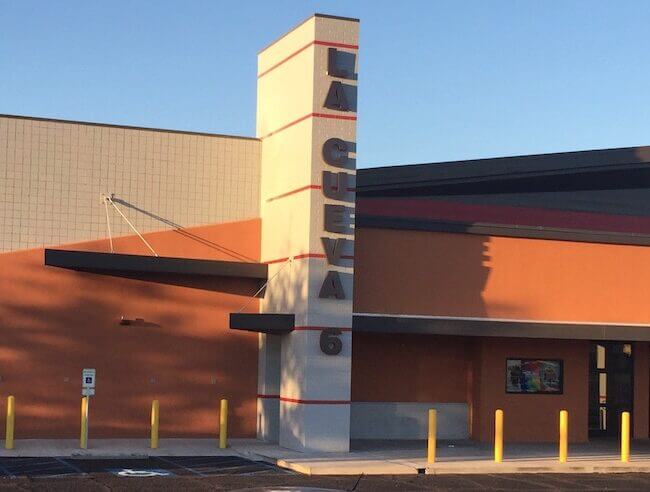 Modern movie theater facade at sunset, featuring a geometric architectural design with orange and cream colors, a tall vertical sign with the word "cinema," and a clear blue sky background.