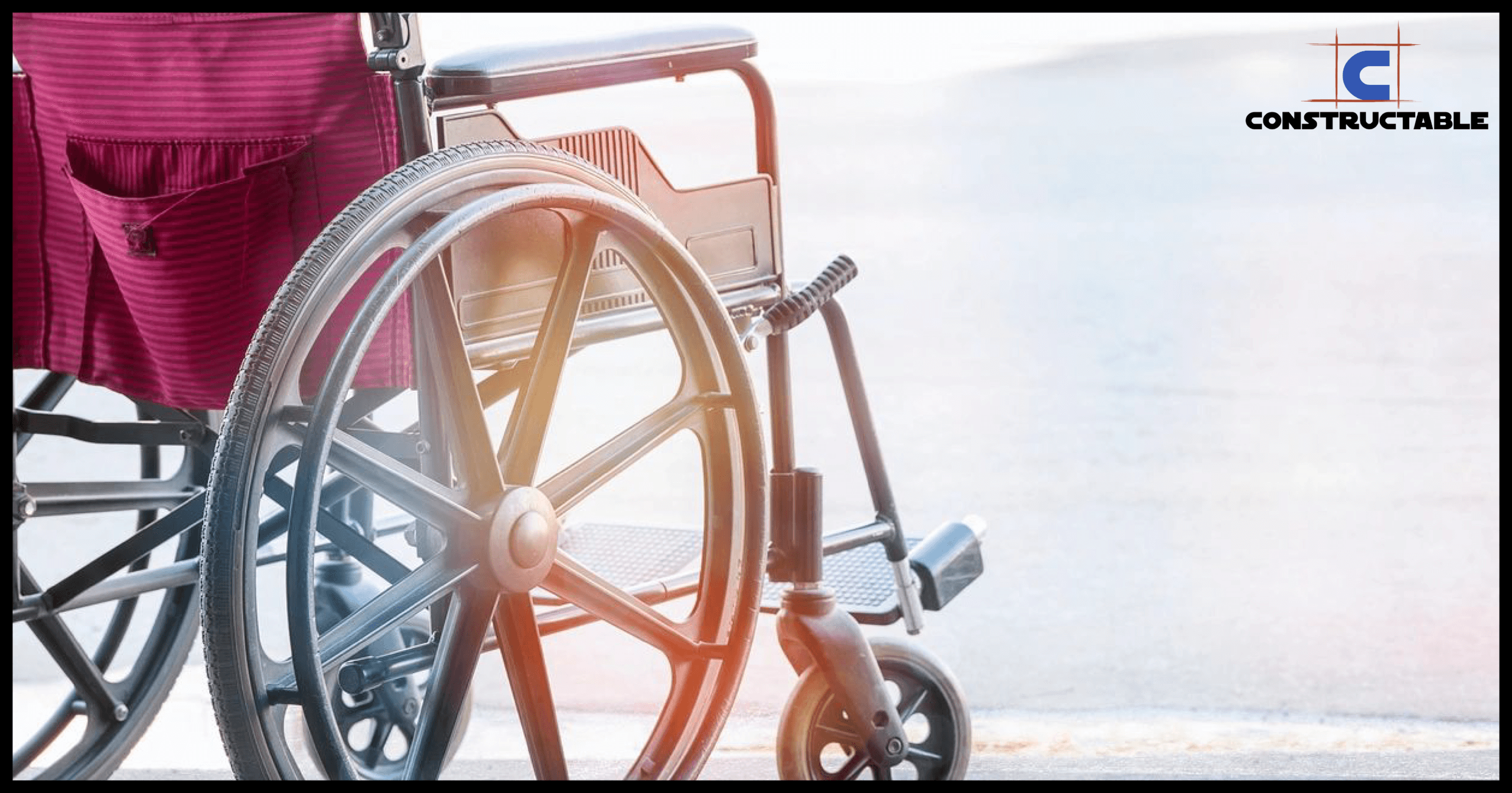 An empty wheelchair in sharp focus with sunlight casting a glow, featuring the construction costs logo on the top right.