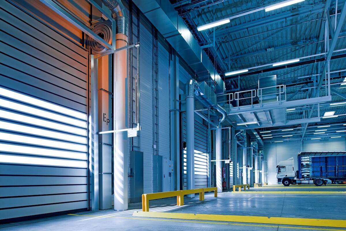 Interior of a modern industrial warehouse with a focus on vibrant blue led lights illuminating the area, large rolling doors, and a truck parked at the loading dock.
