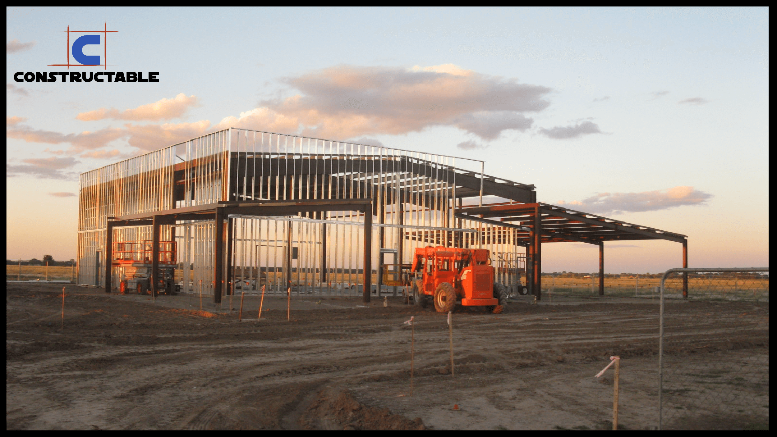 Construction site at sunset with the metal buildings partially erected and a red crane on the left. The company logo “Constructable” appears in the upper left corner.