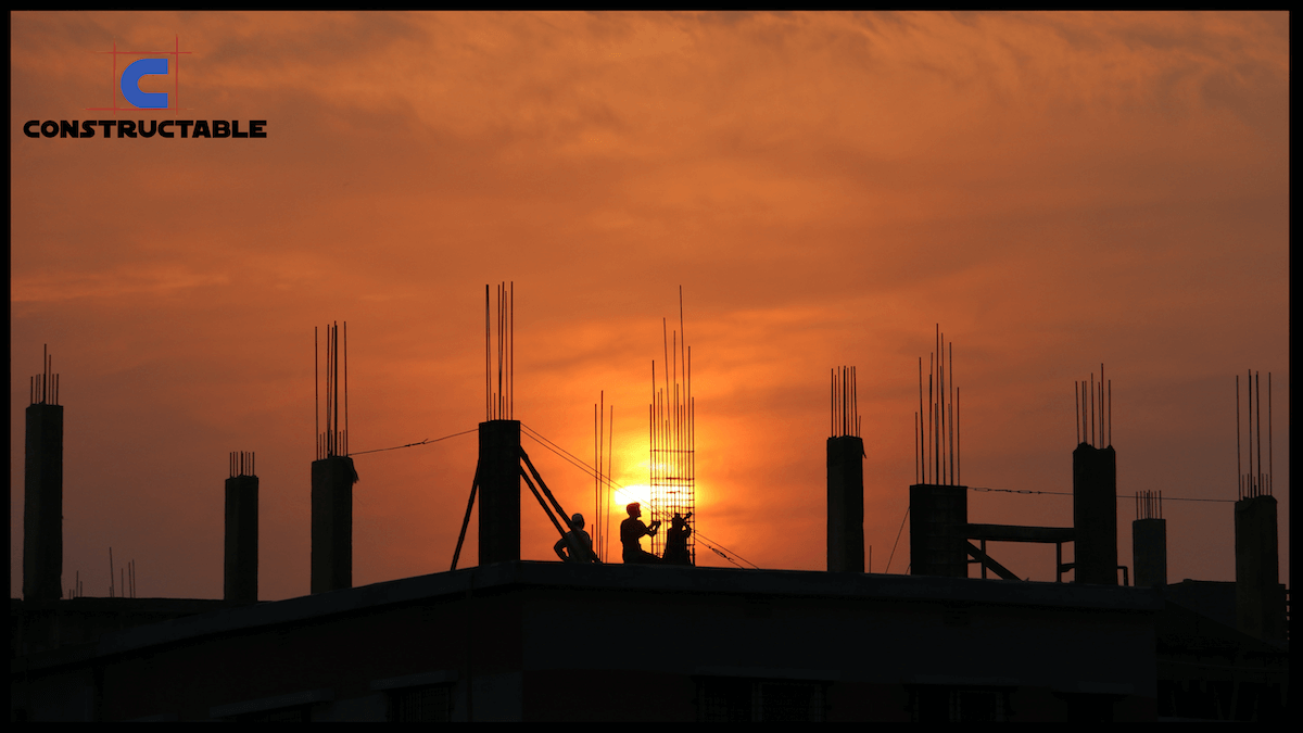 Silhouette of two construction workers on a building site against a vivid sunset, with exposed steel rods and the design logo "constructable" in the corner.
